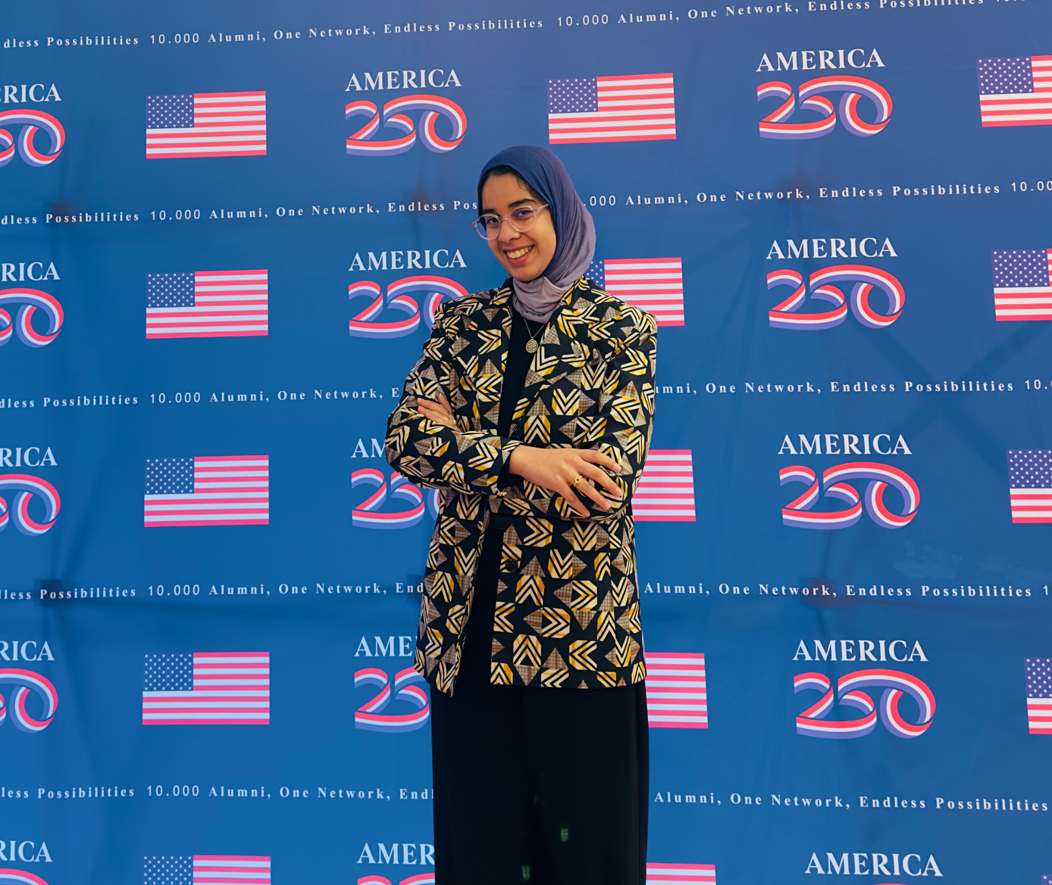 Oumnia wearing a mauve hijab in front of an America 250 alumni event backdrop